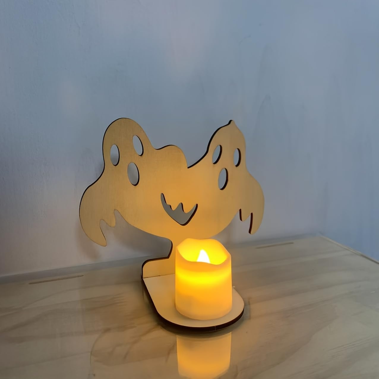 Wooden ghost-shaped candle holder with a lit candle on a wooden surface.