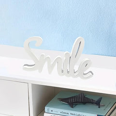 Decorative word 'Smile' on a shelf with books and a shark figurine against a light blue wall.