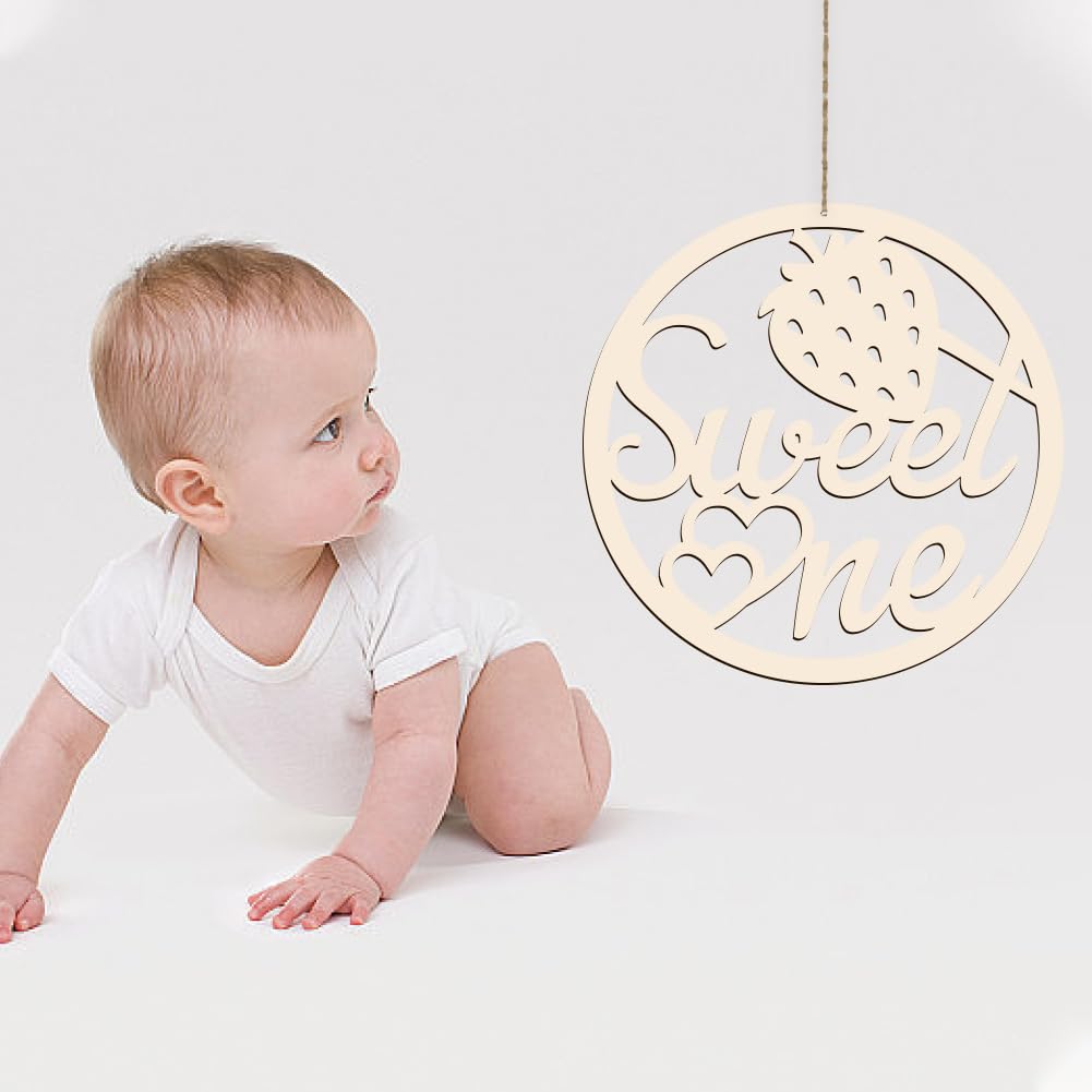 Baby in a white onesie sitting next to a 'Sweet One' decorative sign on a light gray background