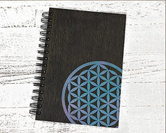 Black notebook with a blue and green flower of life design on a white wooden surface