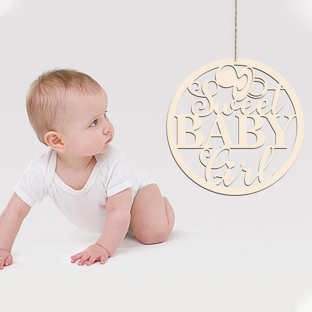 Baby in a white onesie sitting next to a decorative sign with 'Sweet Baby Girl' text on a light background