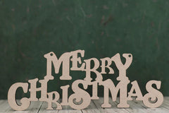 Wooden 'Merry Christmas' letters on a wooden surface with a dark green background