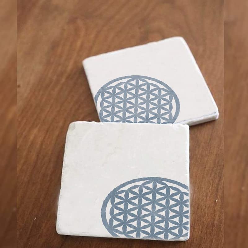 Two white coasters with blue flower of life design on a wooden surface