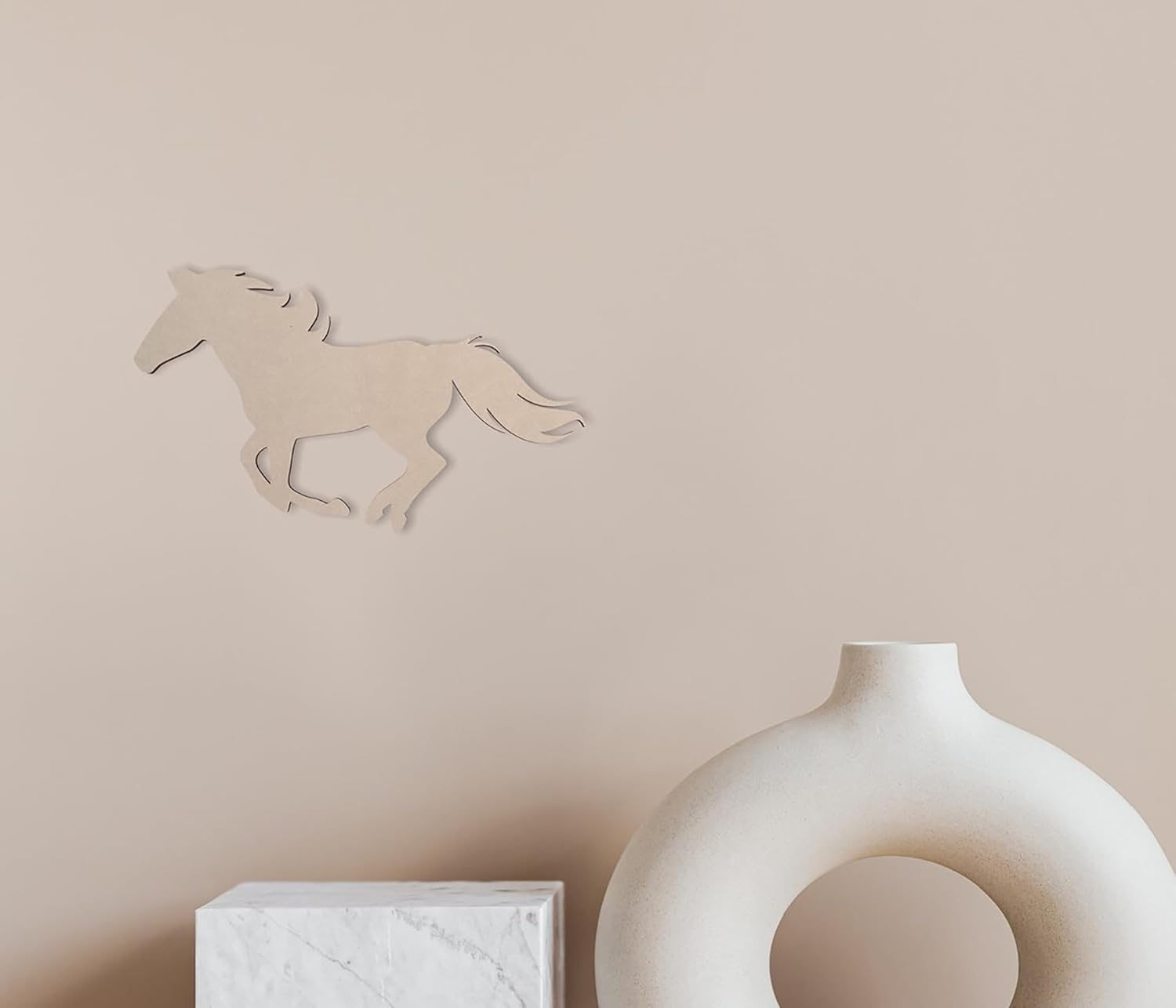 Decorative horse wall art on a beige wall with a white vase and box below.