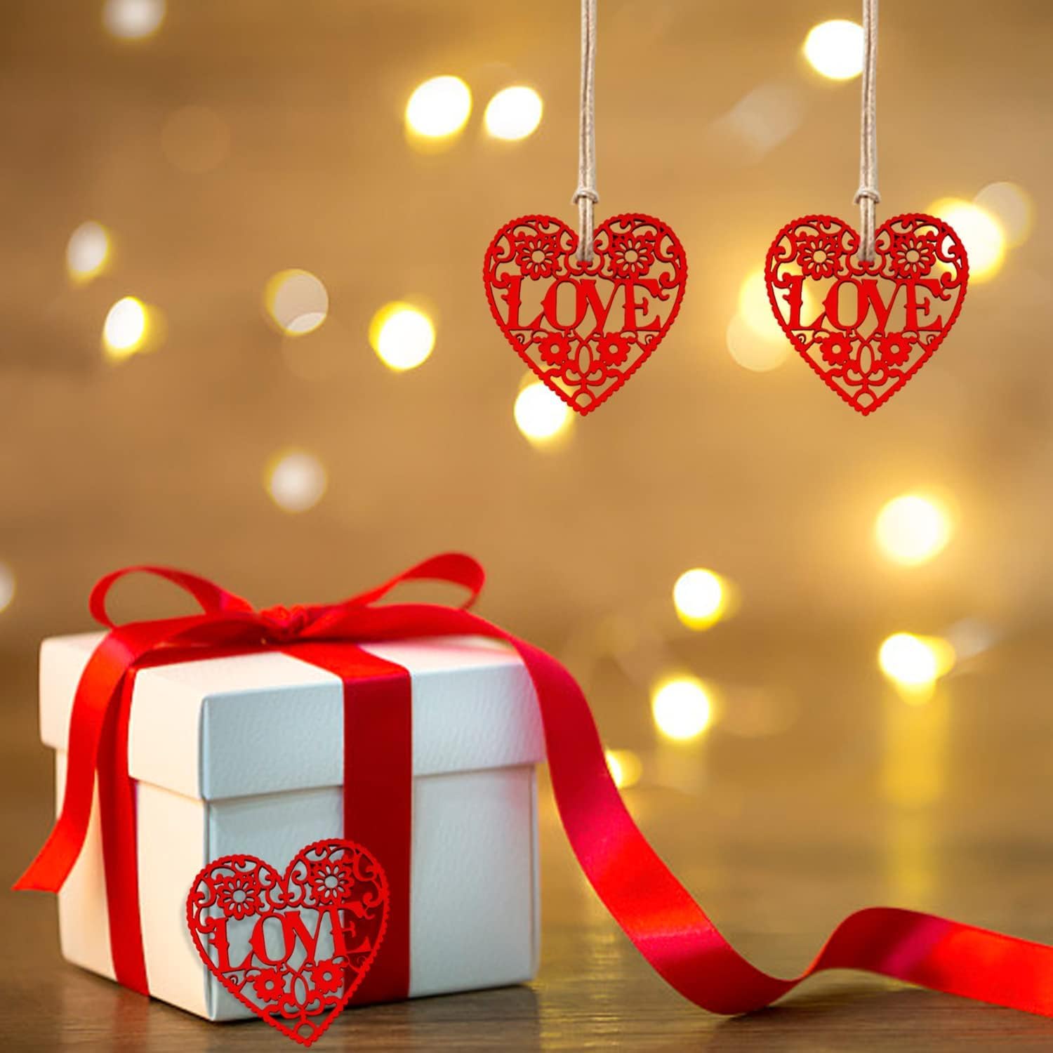 White gift box with red ribbon and 'LOVE' heart decorations against a warm, blurred light background