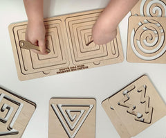Wooden geometric shape sorting puzzle with hands interacting on a white surface