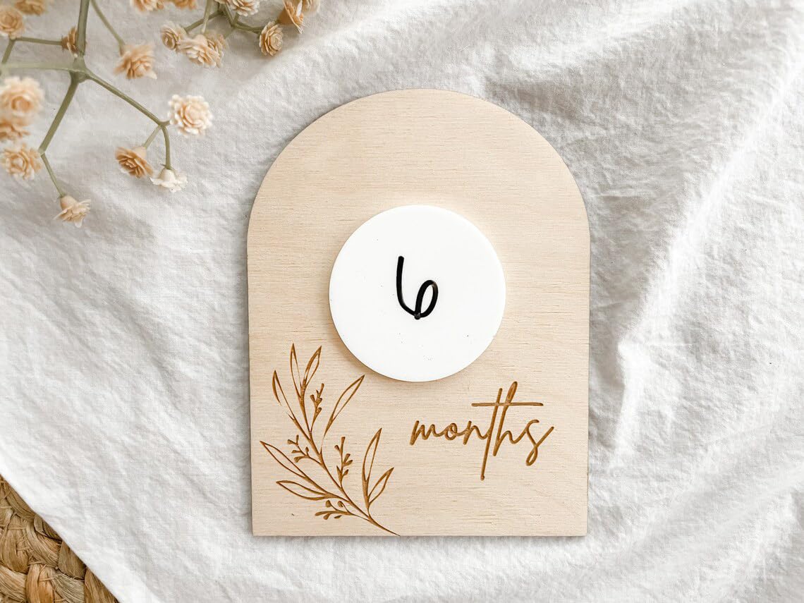 Wooden baby milestone card with '6 months' on a white fabric background