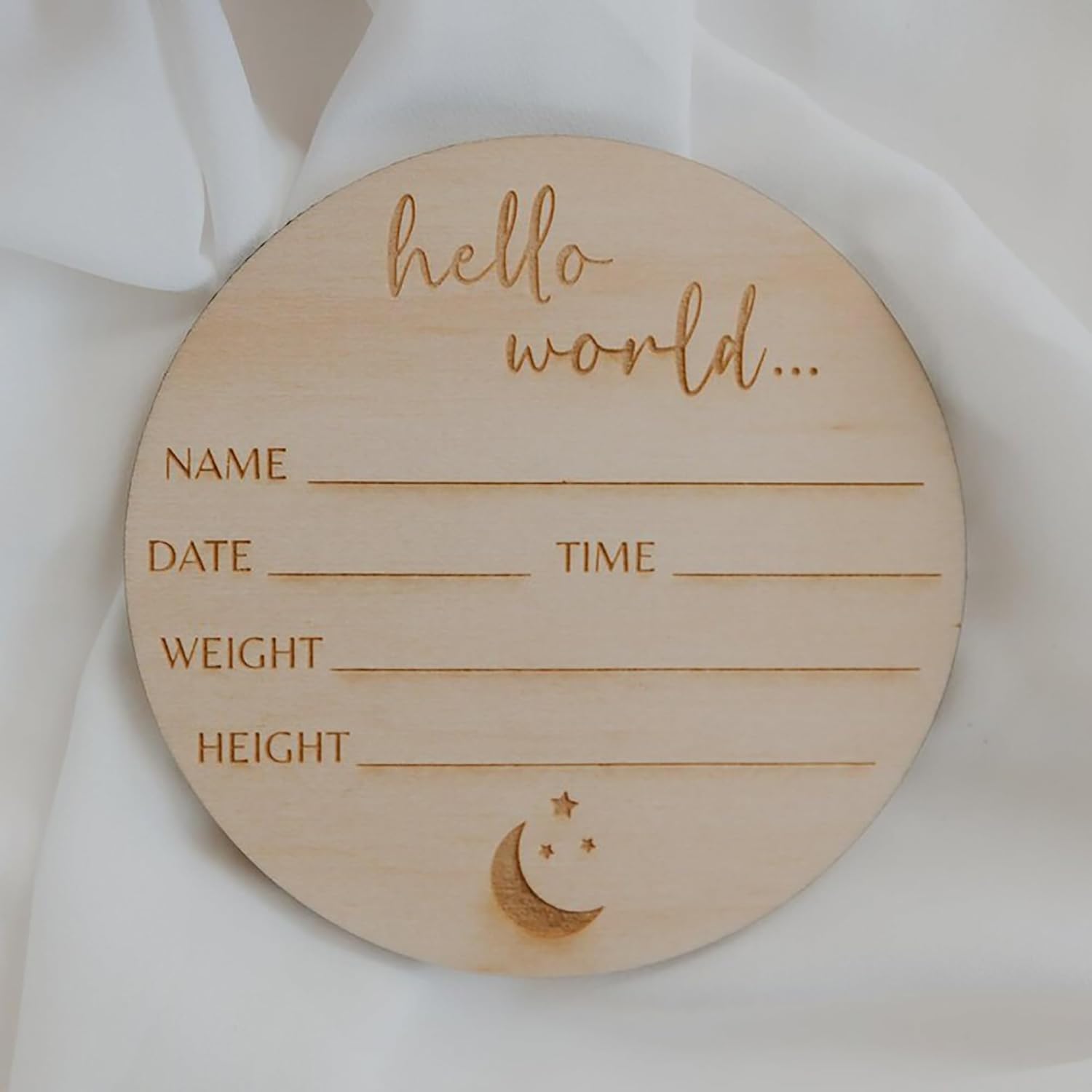 Wooden circular baby milestone marker with engraved text on a white fabric background