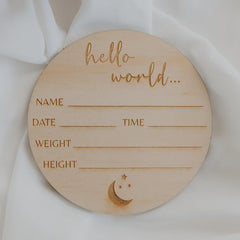 Wooden circular baby milestone marker with engraved text on a white fabric background