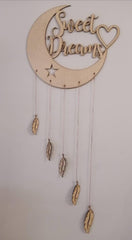 Decorative wall hanging with 'Sweet Dreams' text on a moon shape, featuring feathers and a star.