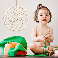 Child holding green beads with a 'Sweet One' decorative sign above