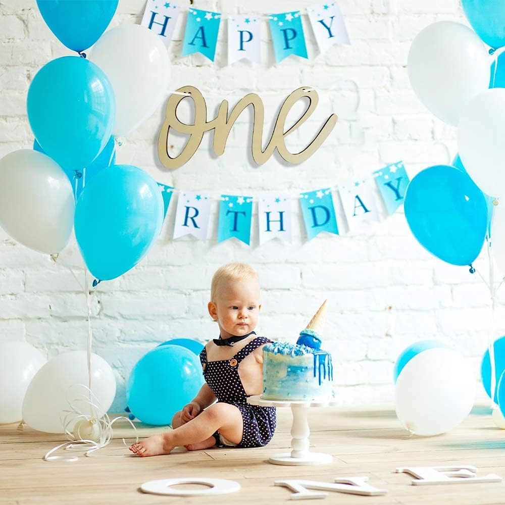 Baby celebrating first birthday with blue and white balloons and 'Happy Birthday' banner.