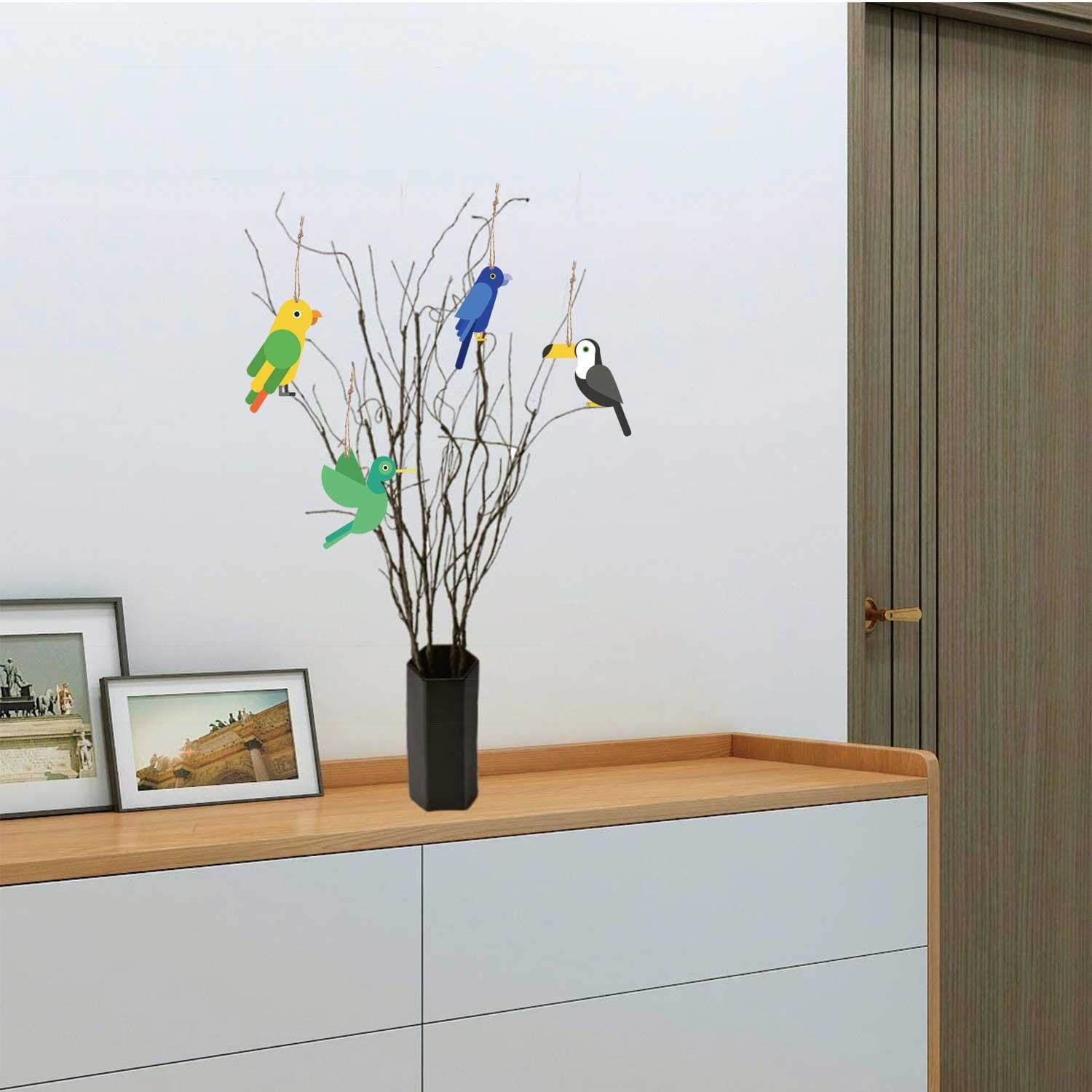 Decorative shelf with a vase containing branches and colorful bird stickers against a light wall.
