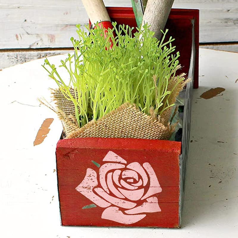 Red wooden box with a pink rose design, containing green plants on a white surface.
