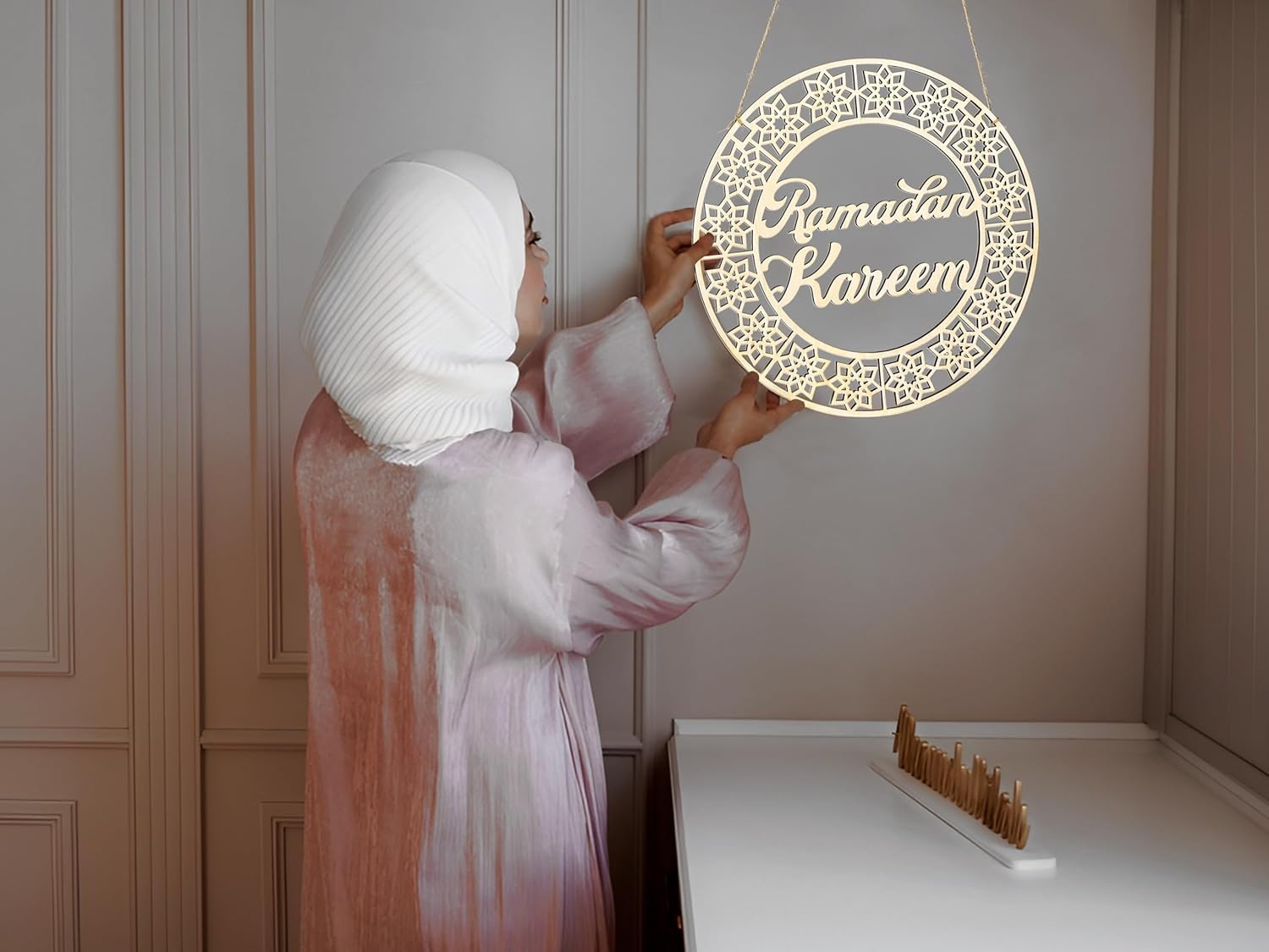 Woman hanging a 'Ramadan Kareem' decorative sign on a wall.
