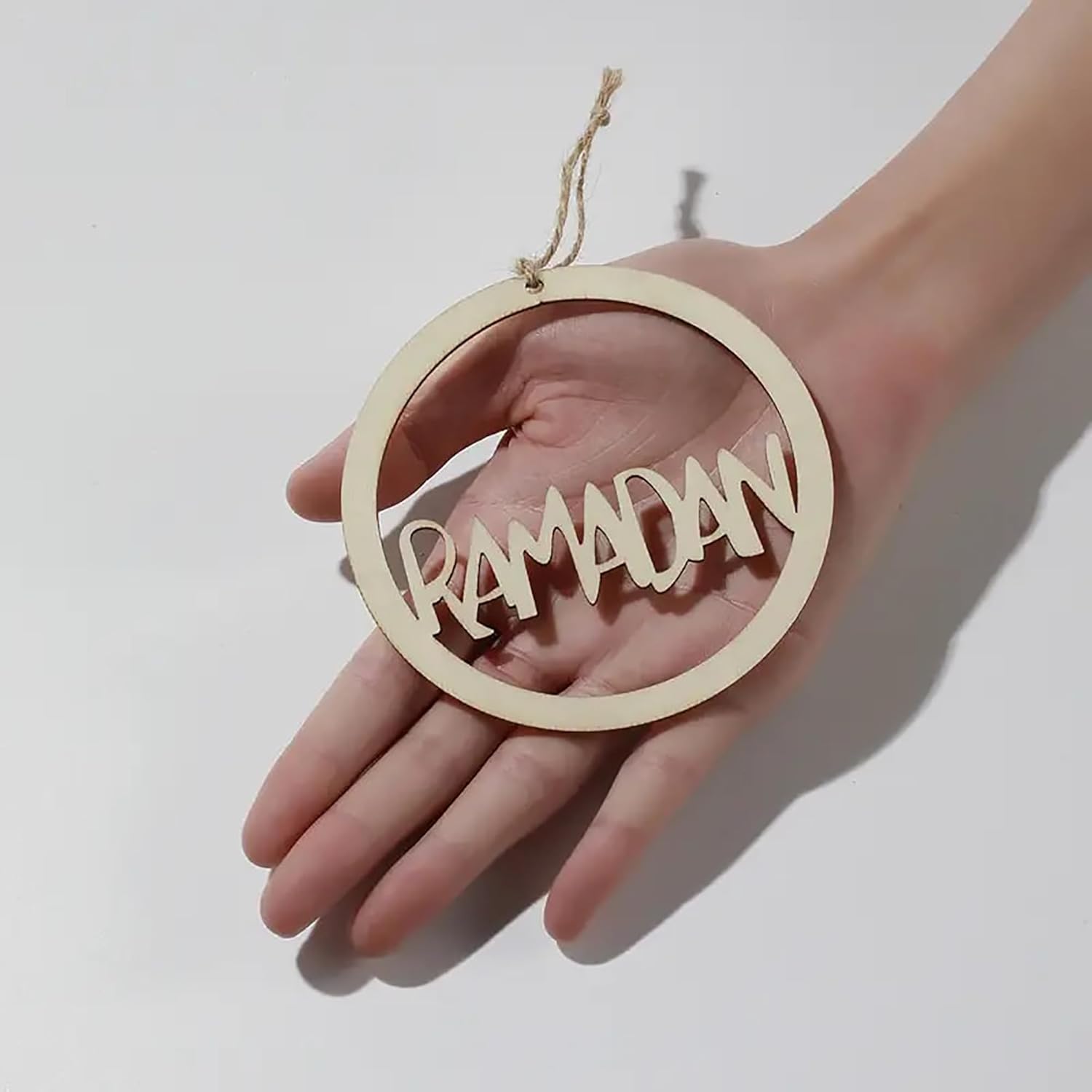 Wooden 'RAMADAN' ornament held in a hand against a white background