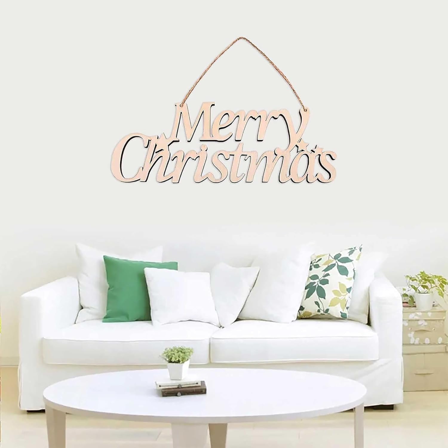 Wooden 'Merry Christmas' decoration hanging above a white sofa with green and patterned cushions.