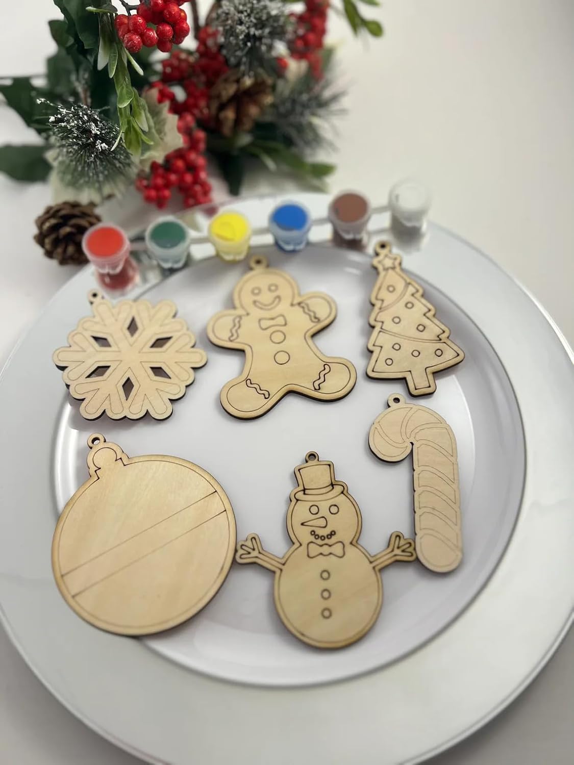 Set of wooden Christmas ornaments on a white plate with paint bottles in the background.