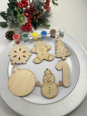 Set of wooden Christmas ornaments on a white plate with paint bottles in the background.