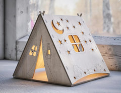 Wooden teepee-shaped lamp with cut-out designs on a wooden surface