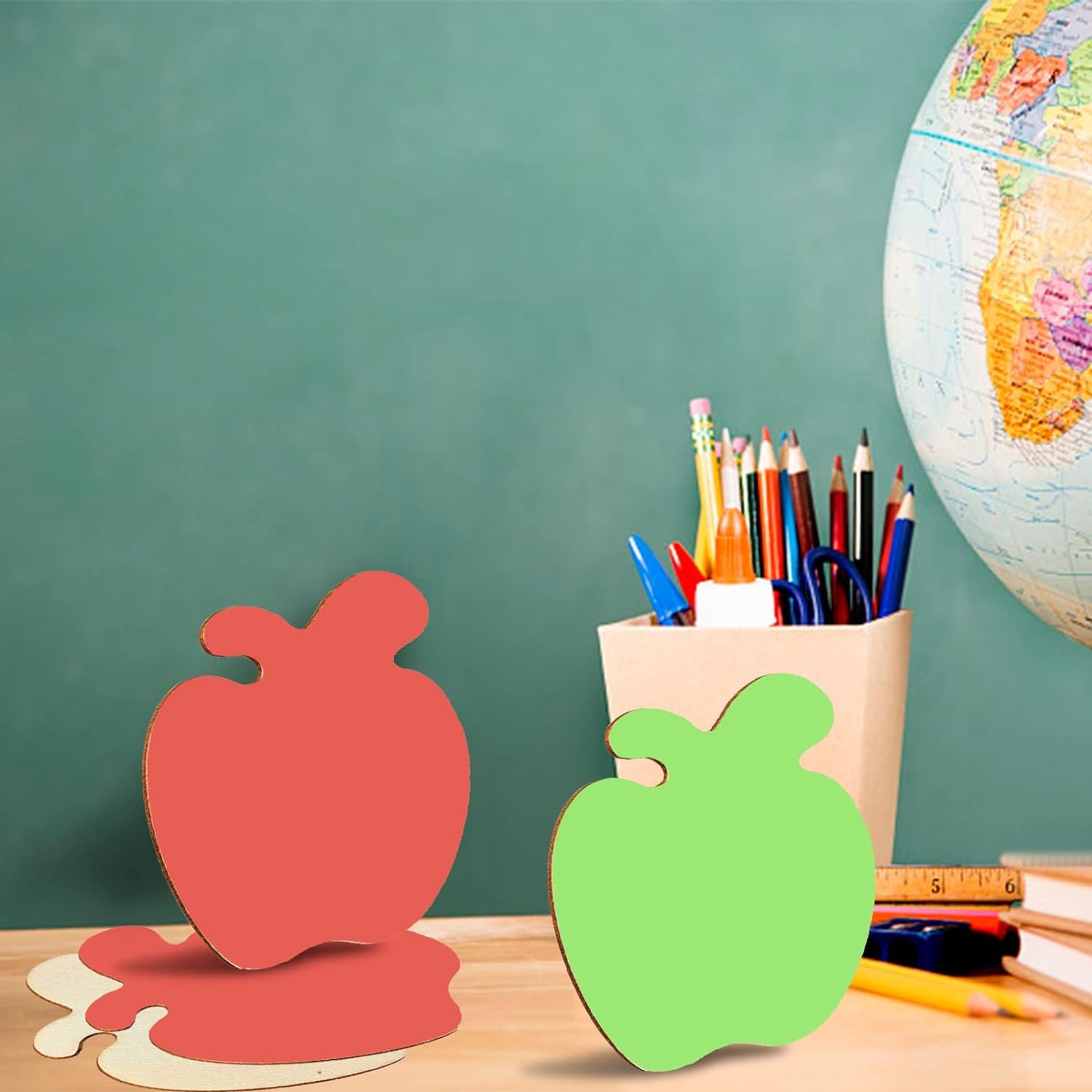Red and green apple-shaped objects on a desk with stationery items and a globe in the background.