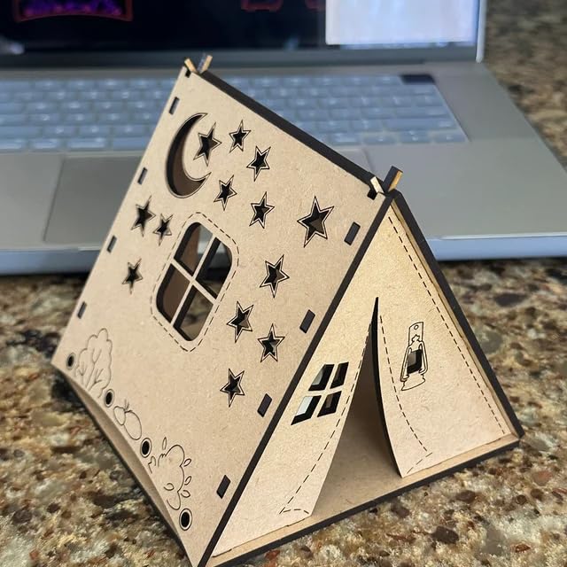 Wooden card with star and moon designs on a countertop in front of a laptop.
