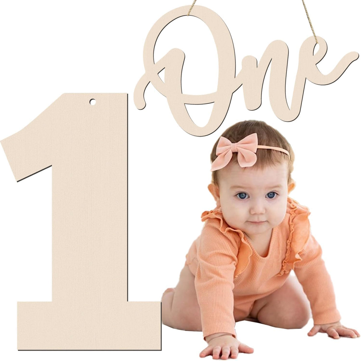 Baby in peach outfit with pink bow and 'One' sign on white background