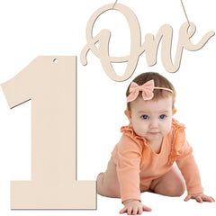 Baby in peach outfit with pink bow and 'One' sign on white background