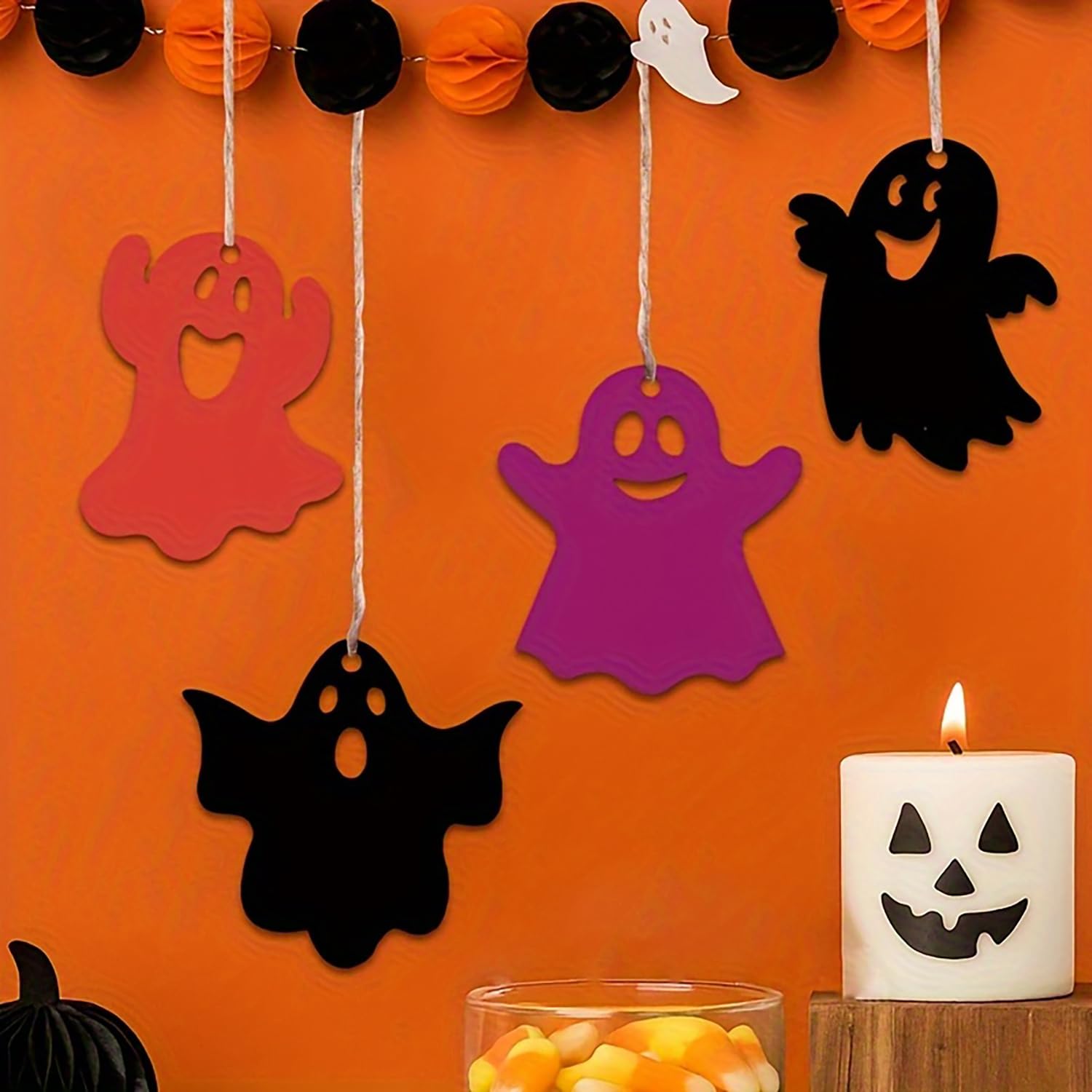 Halloween-themed decorations including colorful ghost cutouts and a jack-o'-lantern candle on an orange background.
