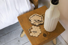 Wooden stool with honeycomb-patterned coasters and a white vase on a wooden floor.