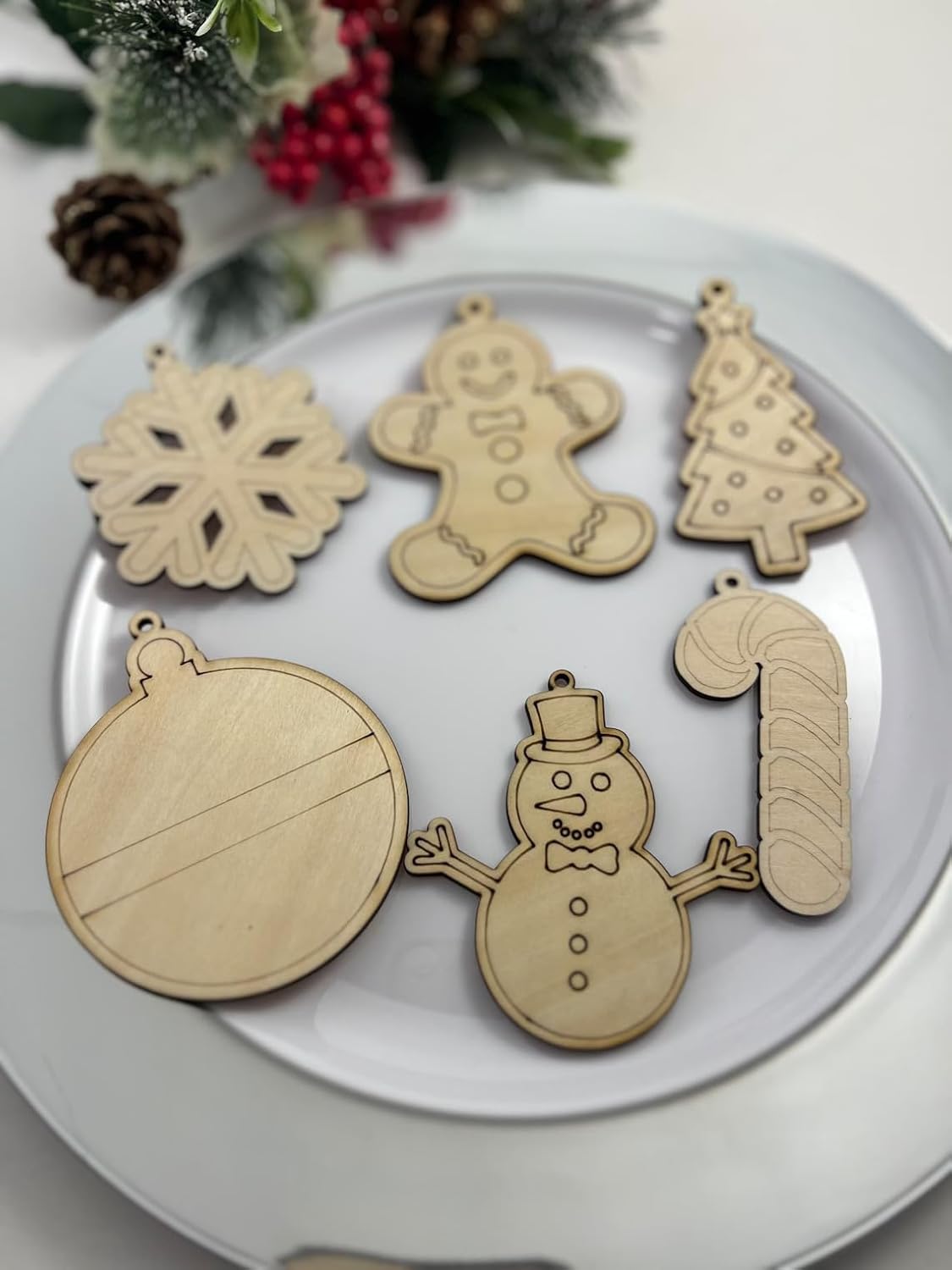 Set of wooden Christmas ornaments including a snowman, gingerbread man, tree, ball, and number '1' on a white plate.