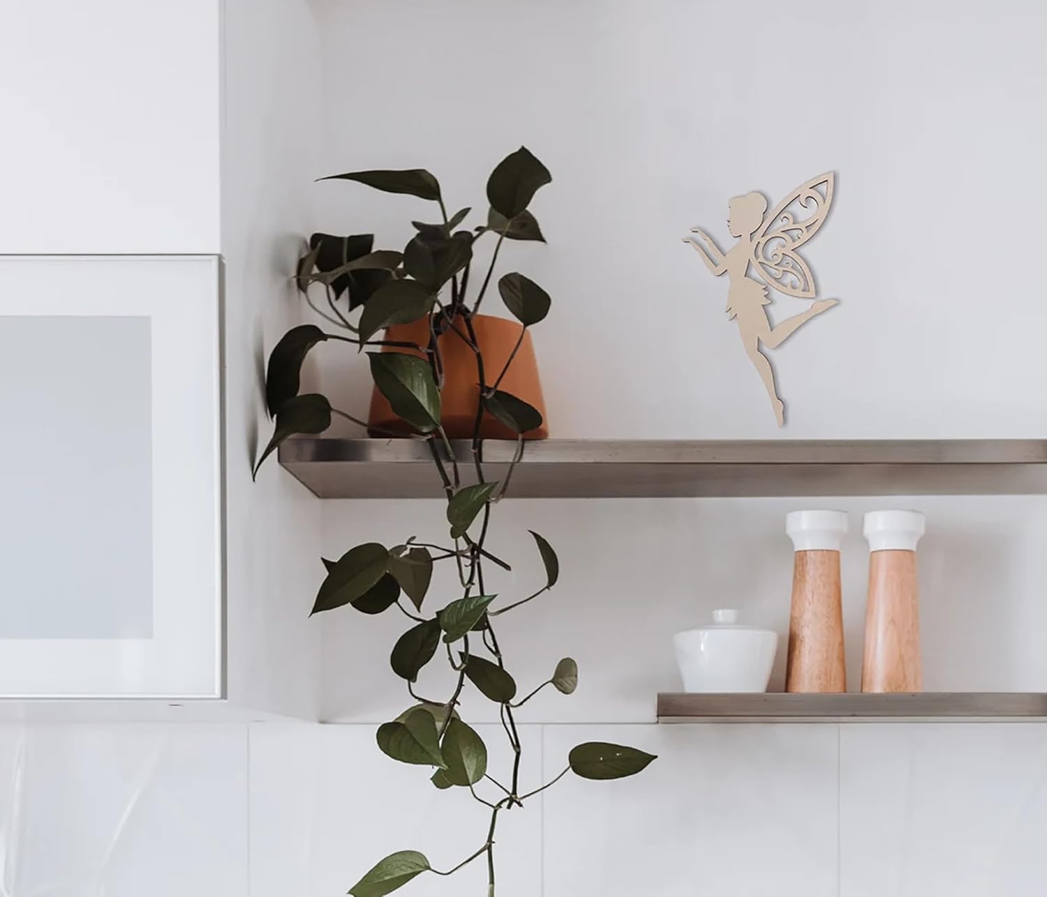 Shelving unit with a plant, decorative fairy figure, and kitchen items on a white wall.
