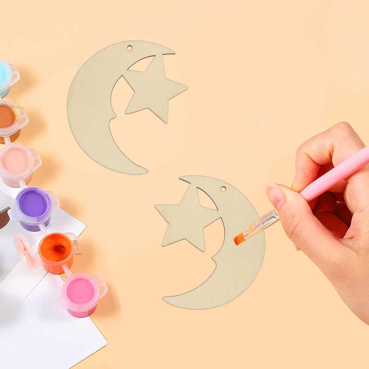 Person painting a star-shaped wooden ornament with a brush on a beige background