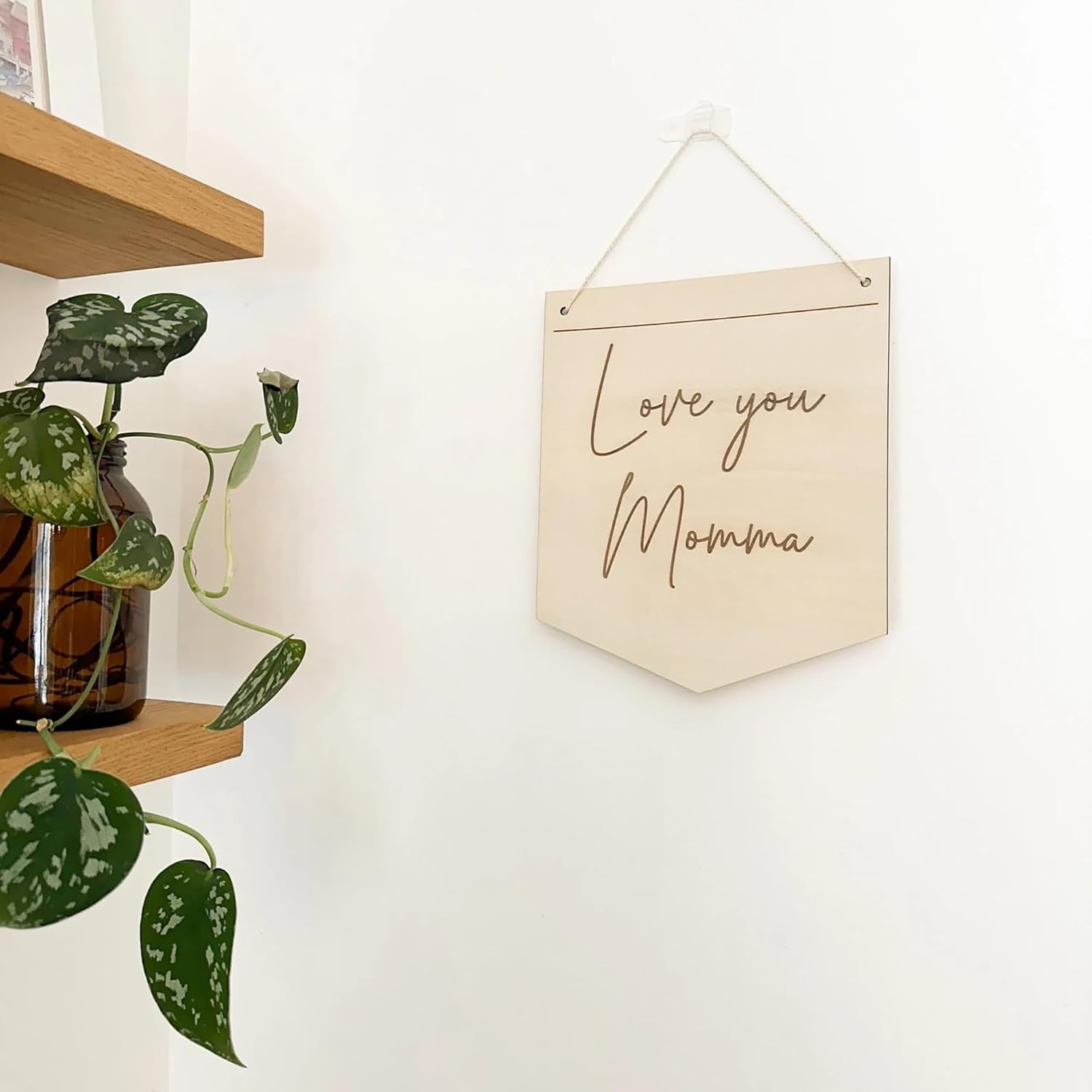 Decorative sign with 'Love you Momma' text hanging on a wall next to a plant.