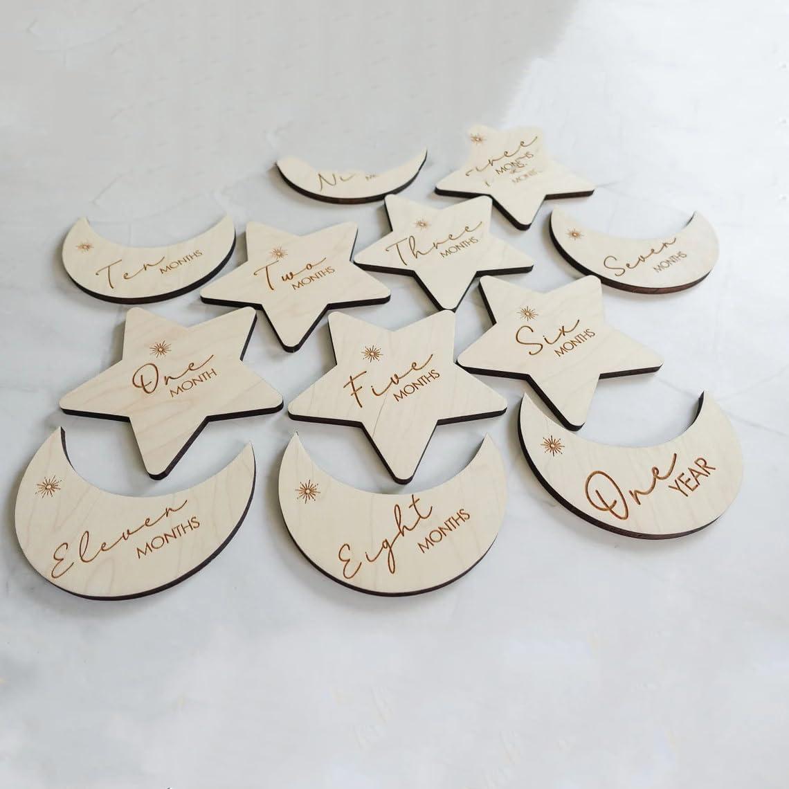 Wooden moon and star-shaped milestone markers with engraved text on a light gray background.