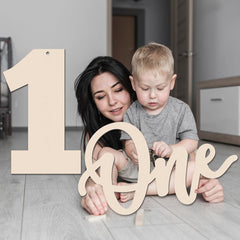 Woman and child with wooden numbers spelling 'One' on a light wood floor.
