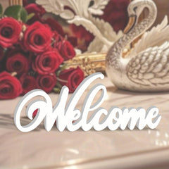 Decorative 'Welcome' sign with red roses and a swan figurine on a reflective surface.