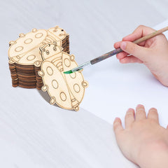 Wooden ladybug shapes with a hand painting one of them on a white surface.