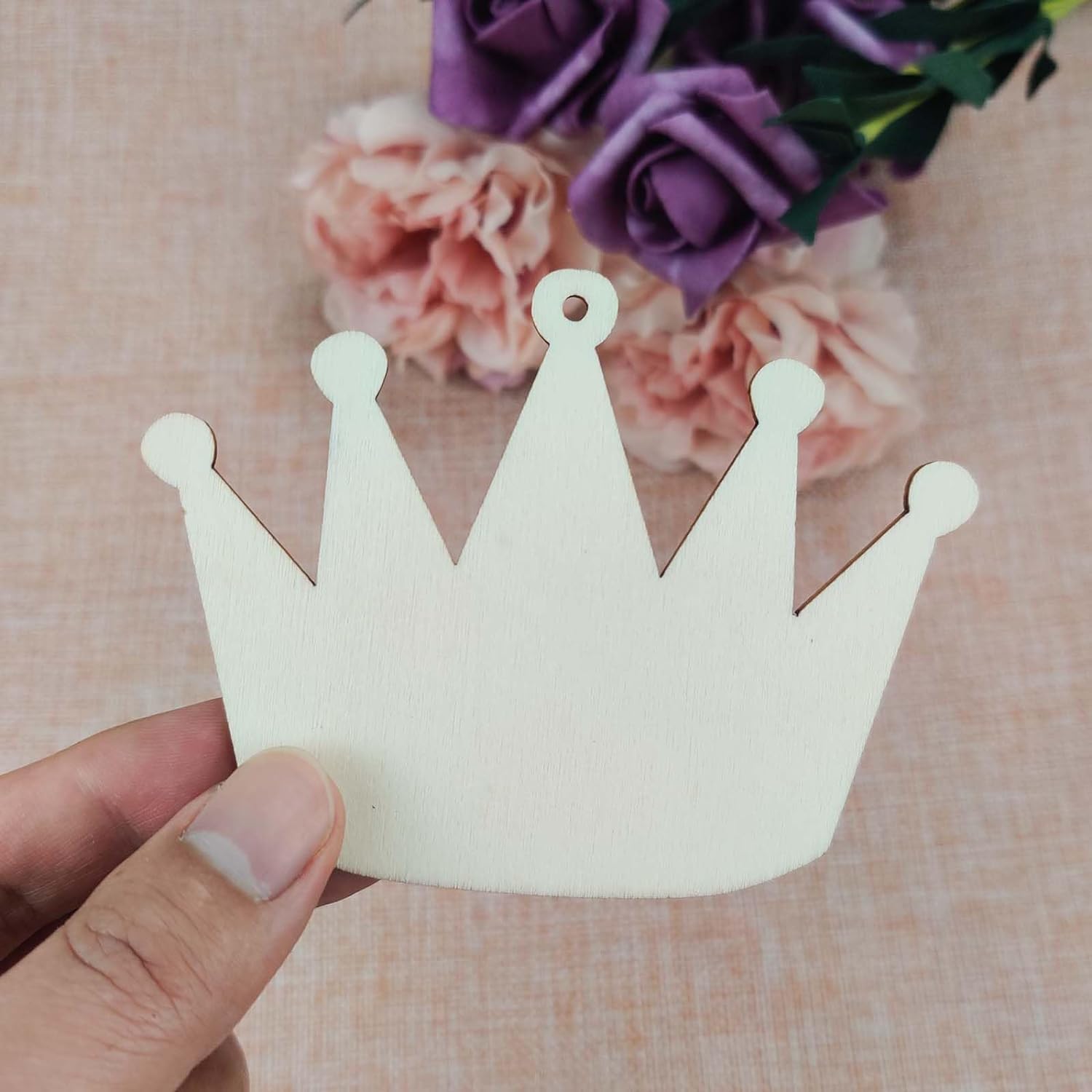 White paper crown held by a hand with flowers in the background