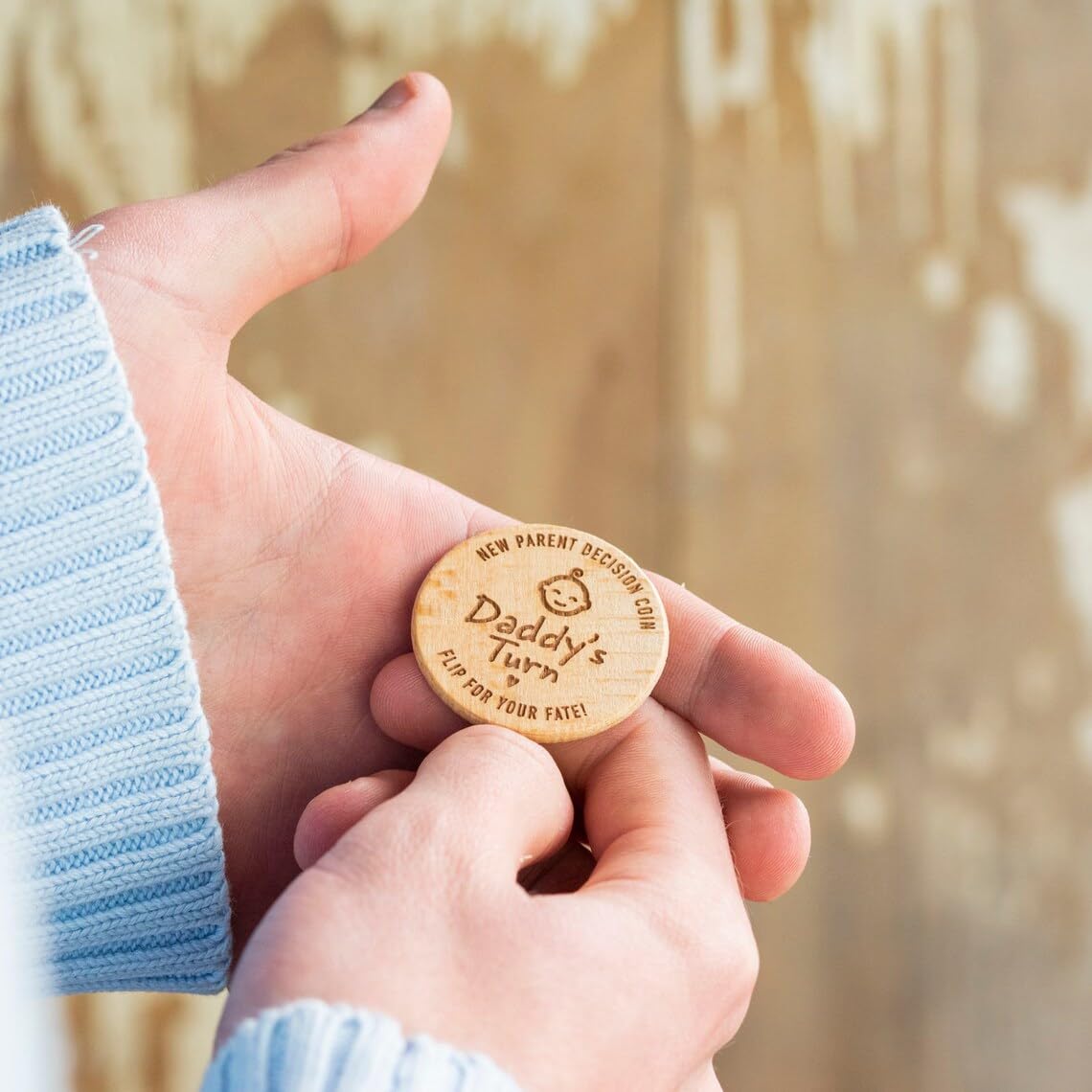 Wooden token with 'Daddy's Turn' text held between two hands against a blurred natural background