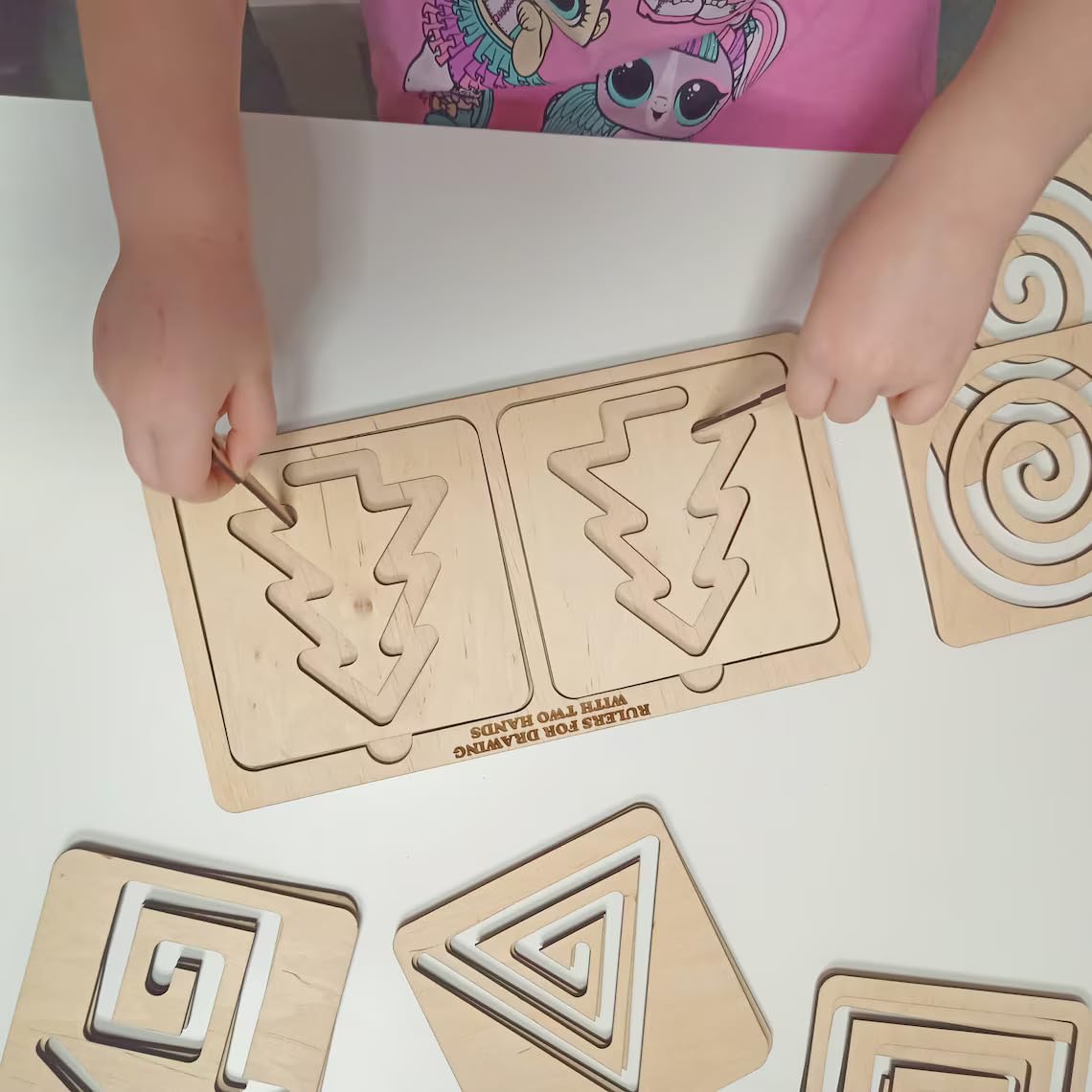 Children's hands interacting with wooden geometric shape sorting boards on a white surface.