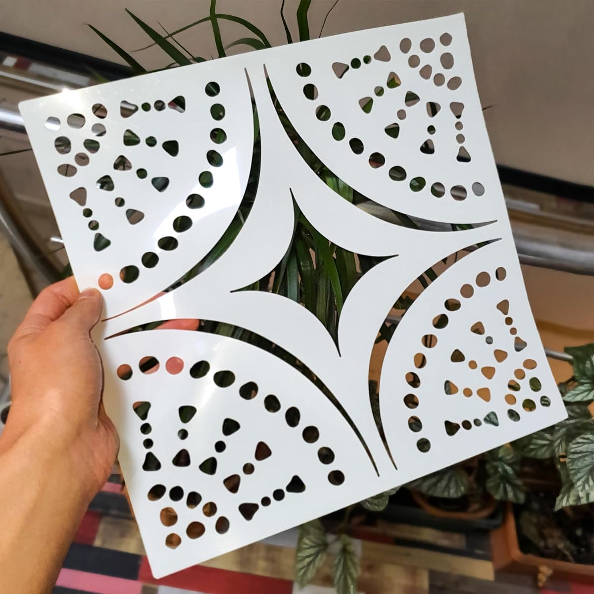 Hand holding a white decorative panel with cut-out patterns against a blurred indoor background