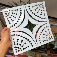 Hand holding a white decorative panel with cut-out patterns against a blurred indoor background