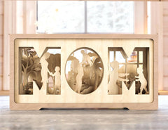 Wooden decorative piece with cut-out silhouettes and 'MOM' text on a wooden surface.
