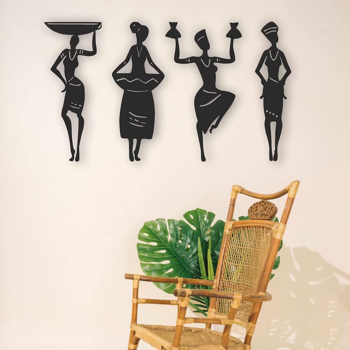Decorative wall art of black silhouettes of women holding items on a white wall with a wicker chair and plant.
