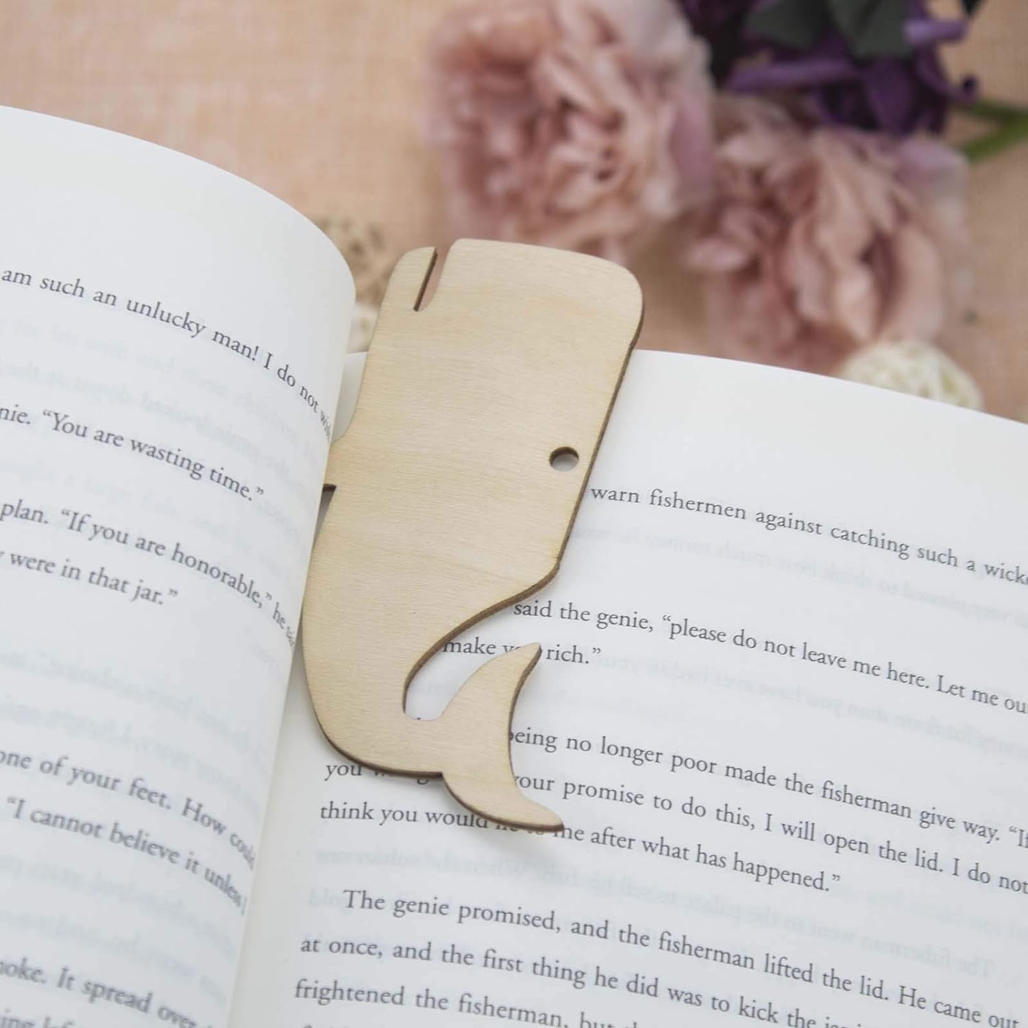 Wooden whale-shaped bookmark on an open book with a blurred floral background