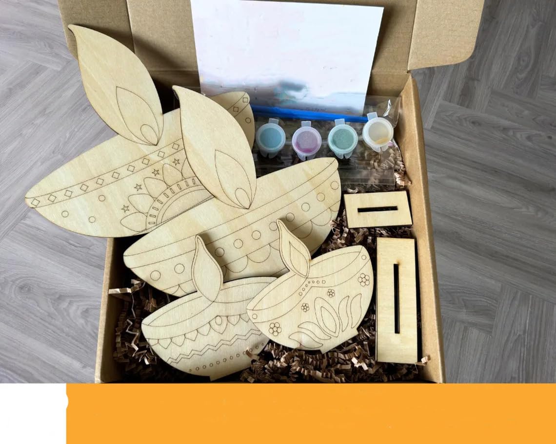 Wooden butterfly craft kit with paint bottles in a cardboard box on a wooden floor.