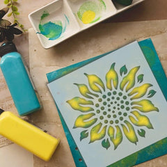 Stenciled design on paper with paint bottles and a palette in the background