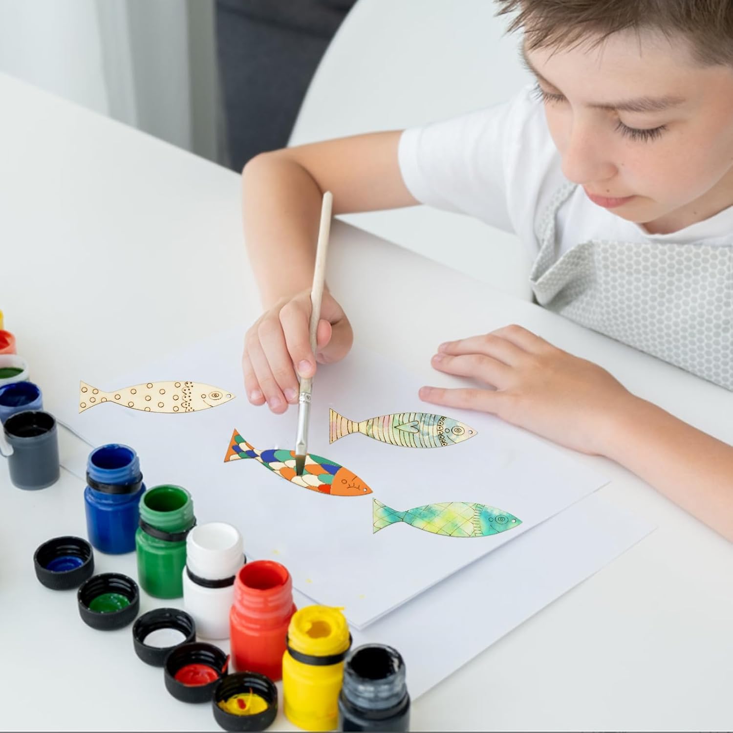 Child painting fish with watercolors on a white surface