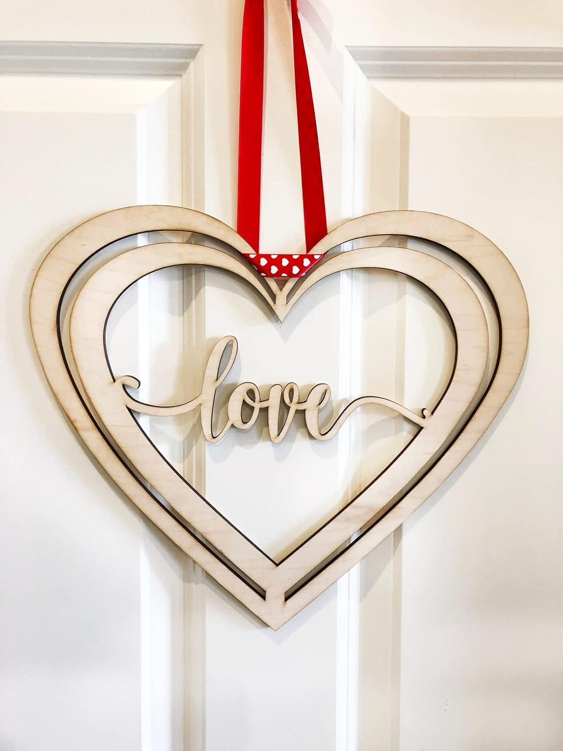 Heart-shaped mirror with 'love' text and red ribbon on a white door
